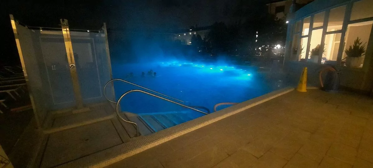 Piscina esterna illuminata di notte con persone.