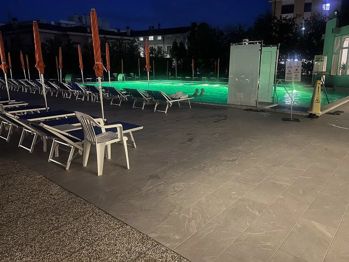 Piscina esterna illuminata di notte con sedie sdraio.
