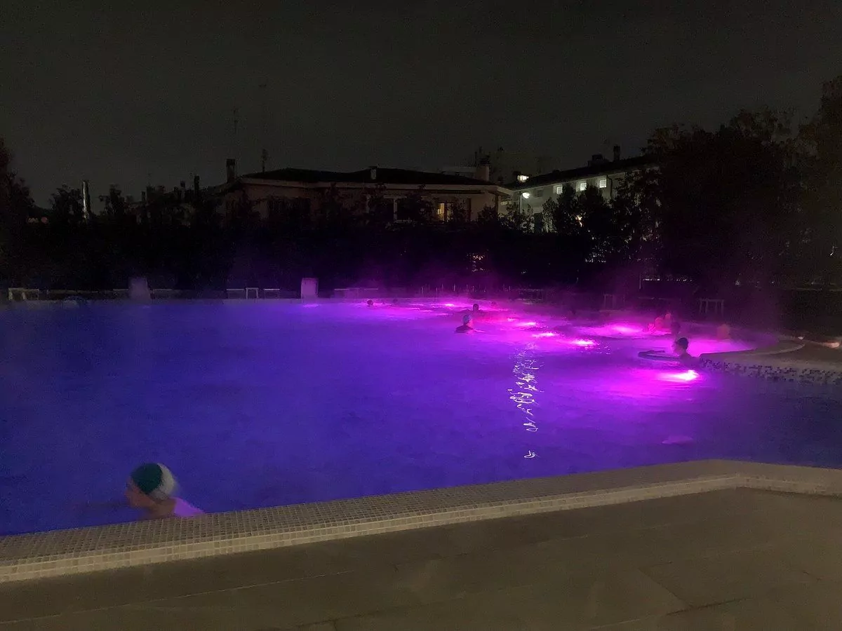 Piscina illuminata di viola di notte con persone.