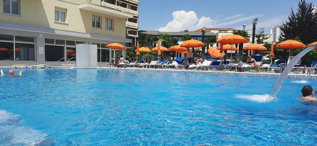 Piscina esterna di hotel con ombrelloni arancioni e persone.