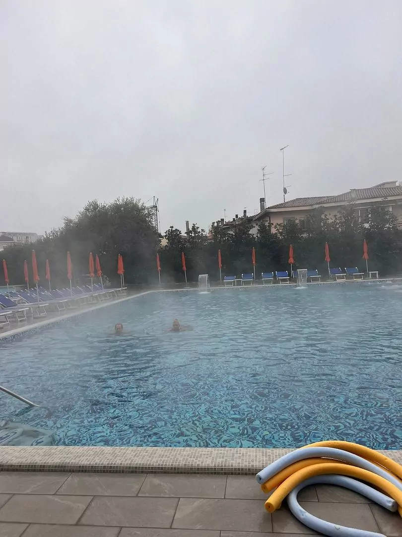 Piscina esterna con ombrelloni chiusi e persone che nuotano.