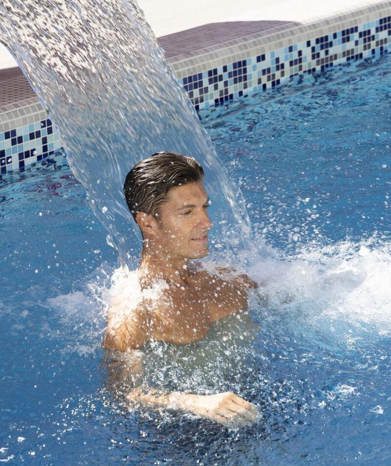 Mann unter einem Wasserfall in einem Thermalbad