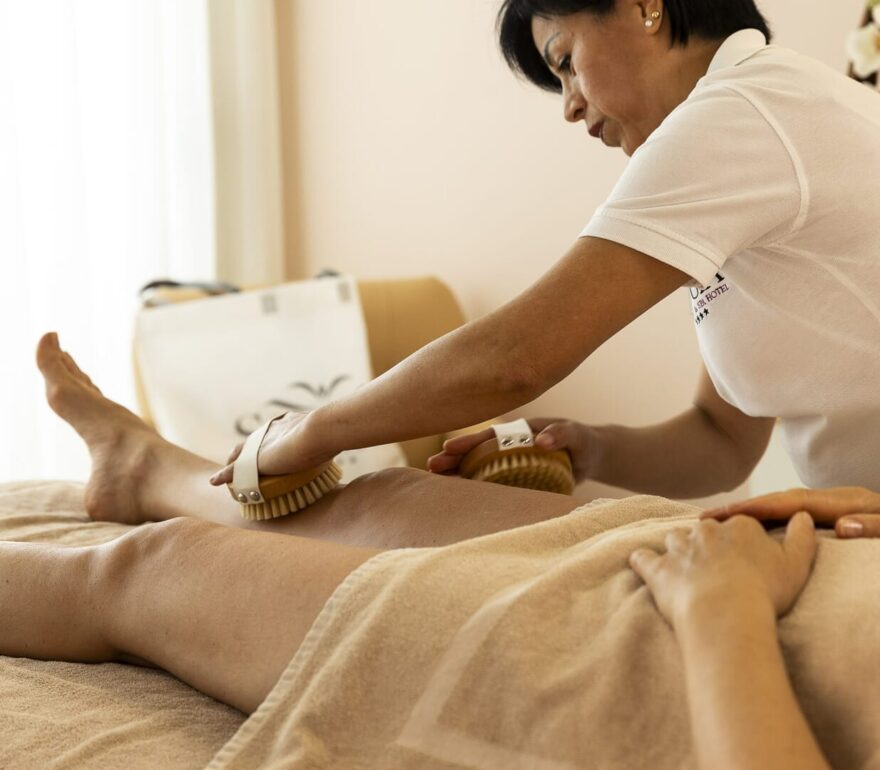 Massage mit einer Bürste am Bein einer Person.