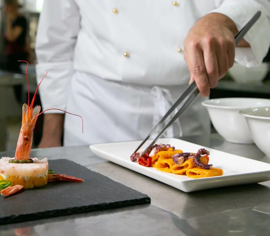 Chef dell’Hotel Savoia Thermæ & Spa di Abano Terme impiatta un piatto gourmet con pesce, verdure e tartare di gamberi in cucina professionale.